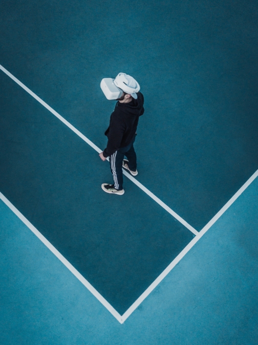 Ein Mann auf einem blauen Tennisplatz trägt eine VR Brille.