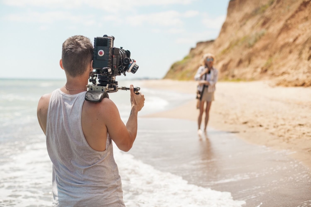 Ein Kameramann filmt eine Frau bei einem Werbefilm-Dreh am Strand.
