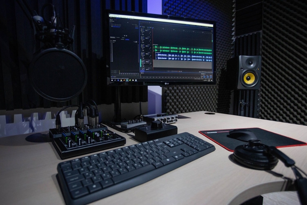 Podcast Studio mit Mikrofon, Kopfhörern, schallisolierten Wänden, Lautsprechern und PC mit Schnittsoftware.