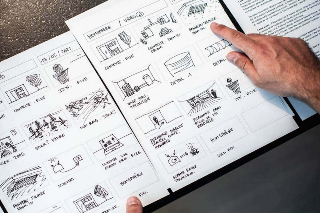 Ein Mann zeigt auf Zeichnungen in einem Buch, das das Storyboard für sein Tutorial Video beinhaltet.