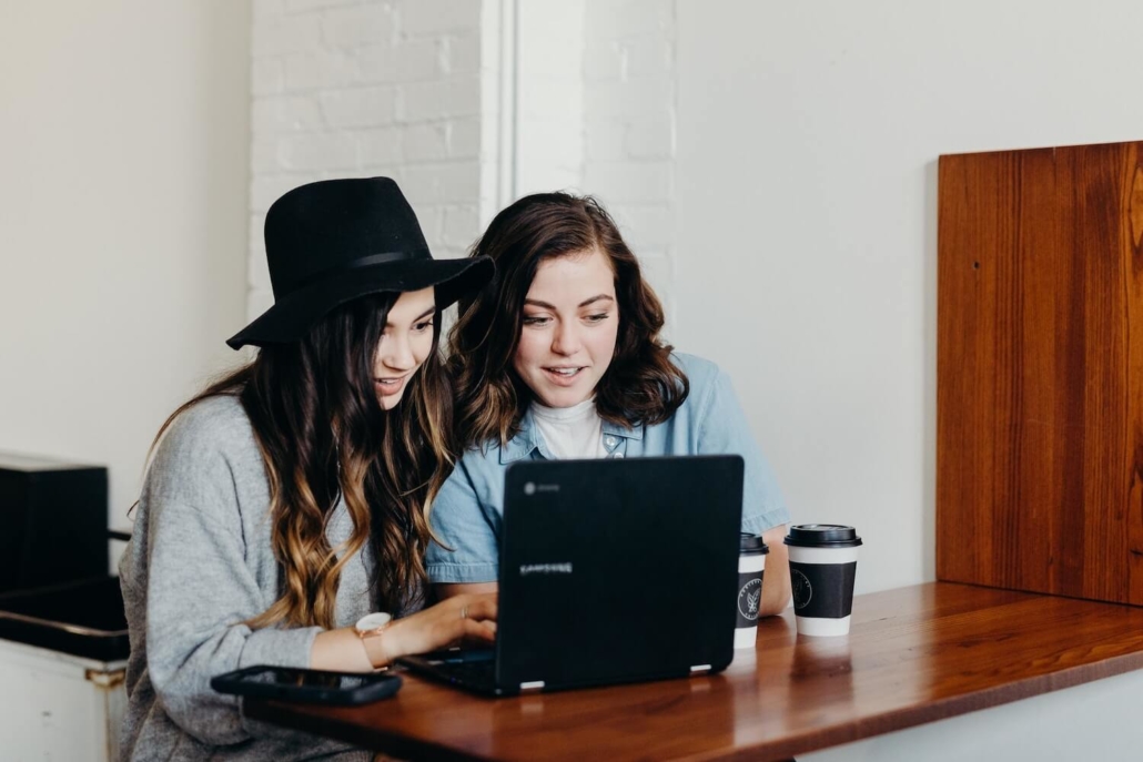 Zwei Frauen sitzen vor einem Laptop und schauen sich ein Video an, das auf einer Website eingebunden wurde.