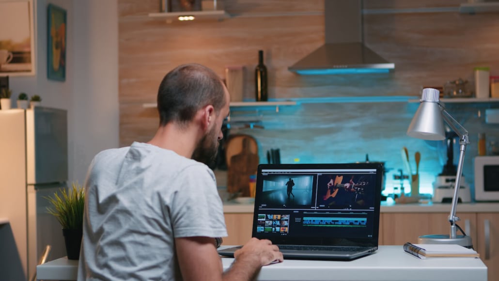 Ein Mann sitzt an einem Schreibtisch und bearbeitet einen Videokurs an seinem Laptop.