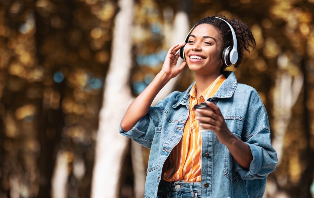 Eine Frau mit Kopfhörer hört bei einem Spaziergang einen Audio Podcast.
