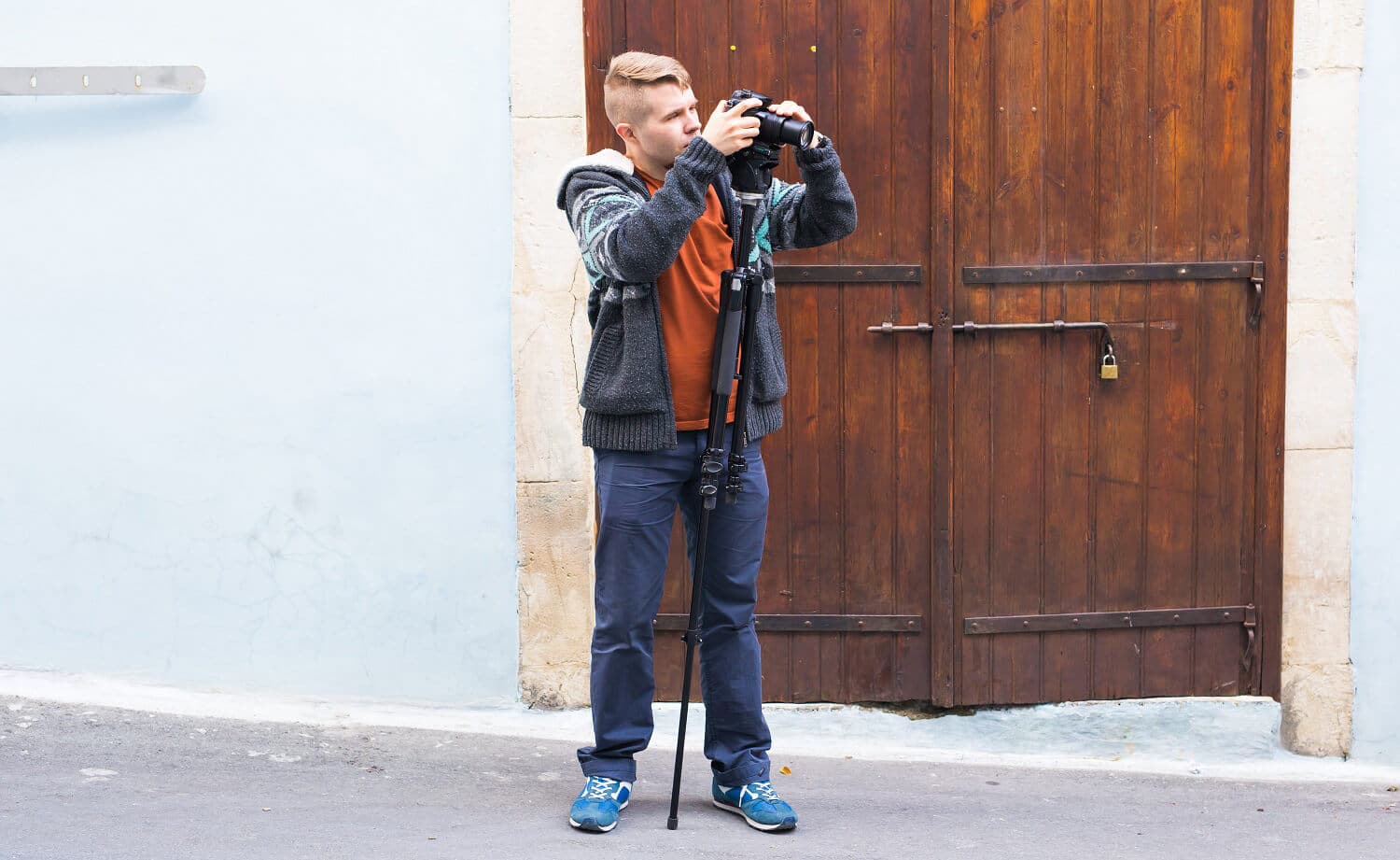 Ein junger Fotograf mit einem ausgefahrenen Einbeinstativ vor blauer Hauswand.