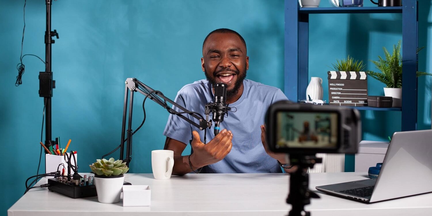 Mann mit Mikrofon vor blauer Wand nimmt einen Video Podcast auf.