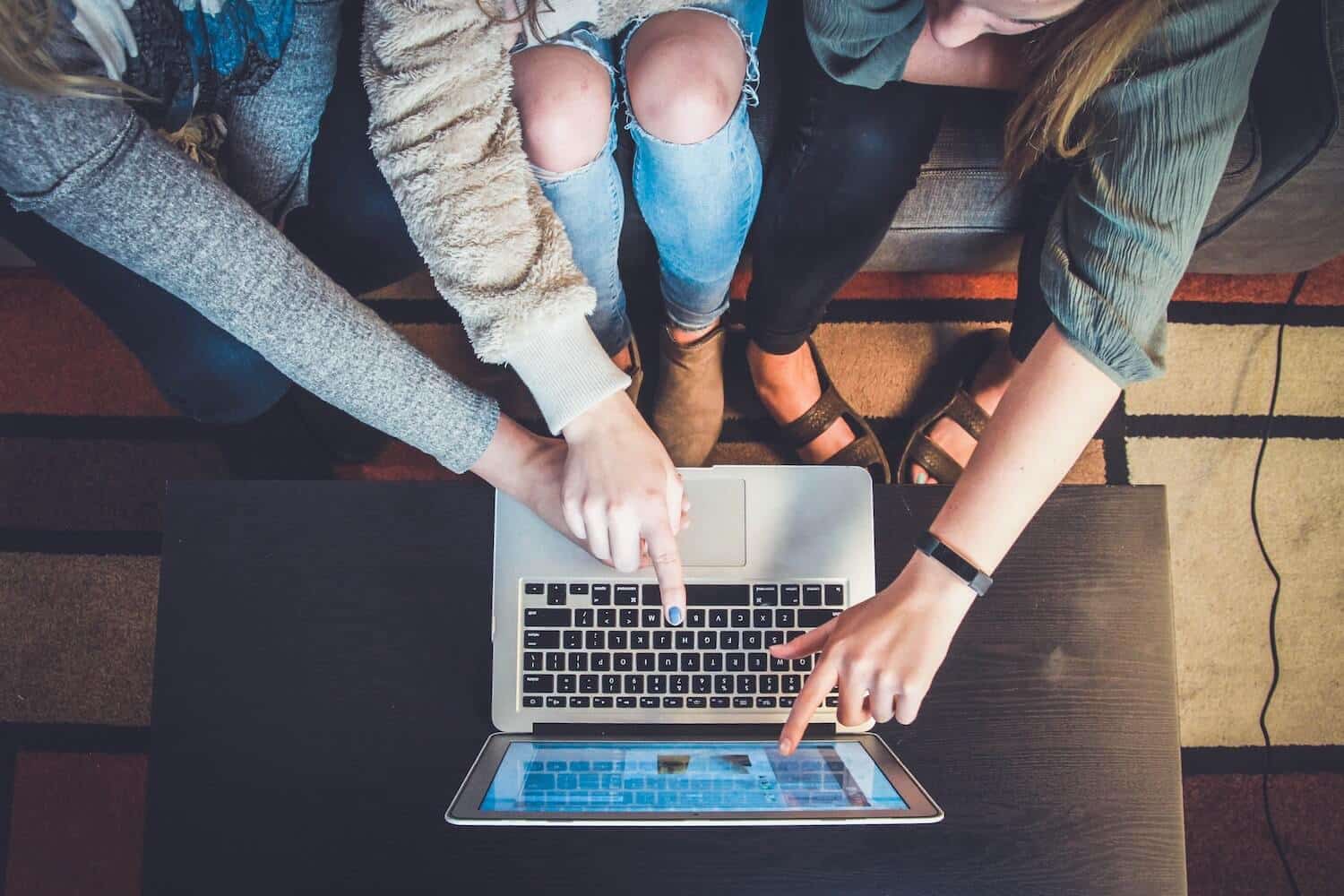 Drei Frauen zeigen auf den Bildschirm eines Laptops und suchen nach aktuellen TikTok Trends.