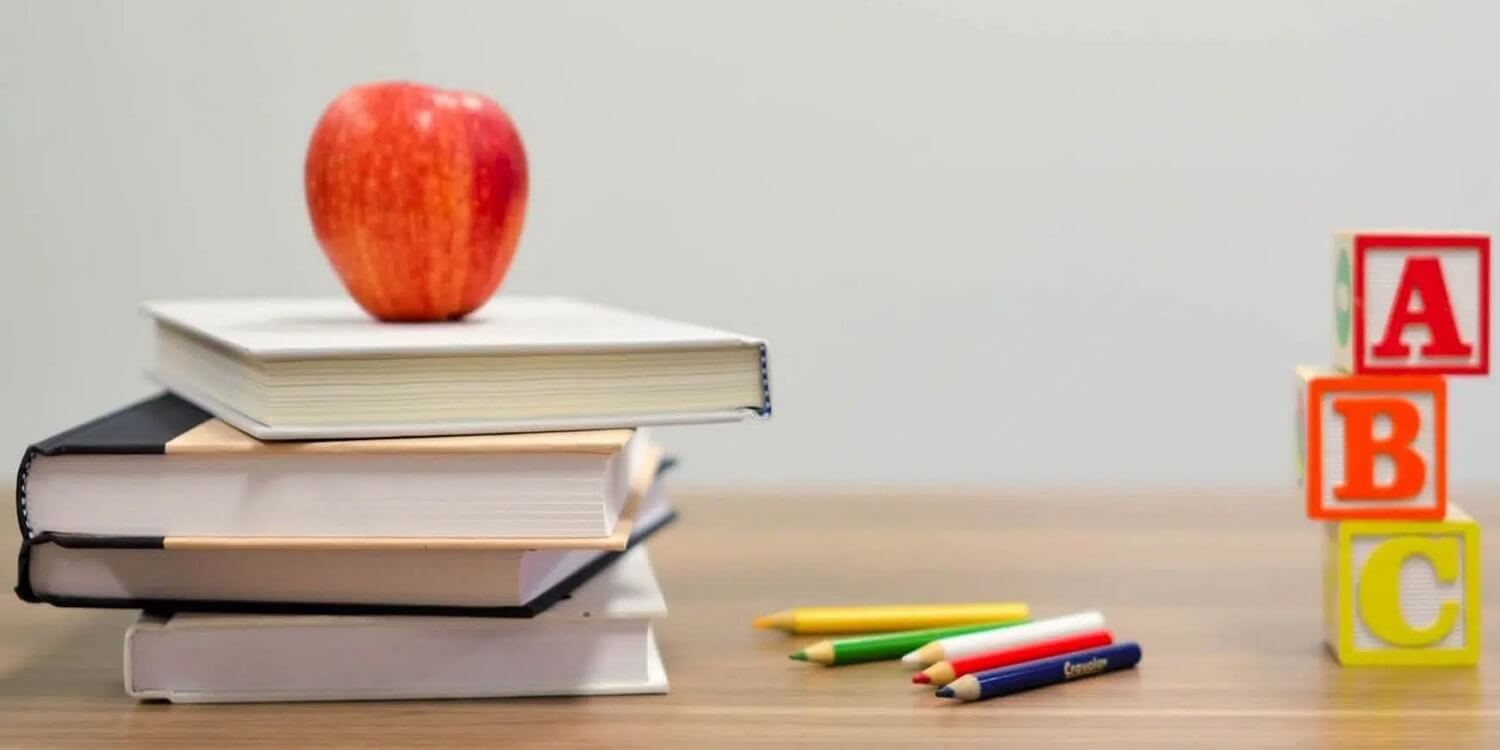 Bücher, Stifte, ein Apfel und Buchstaben liegen auf einem Schultisch.