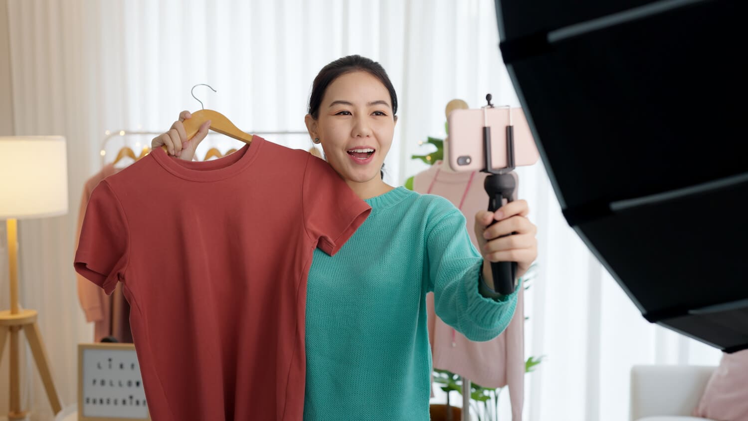 Eine Frau hält ein rotes T-Shirt in einer und eine Kamera in der anderen Hand.