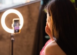 Eine Frau sitzt vor einem Smartphone und einem Ringlicht und erstellt ein Instagram Video.