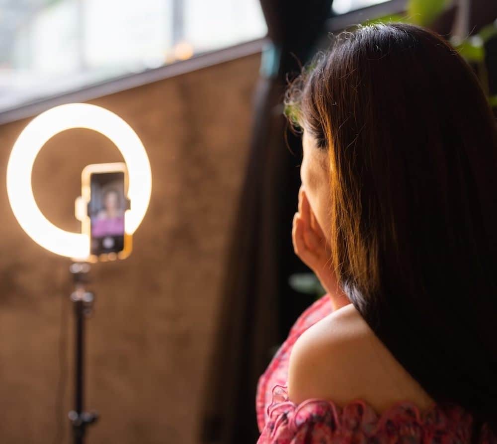 Eine Frau sitzt vor einem Smartphone und einem Ringlicht und erstellt ein Instagram Video.