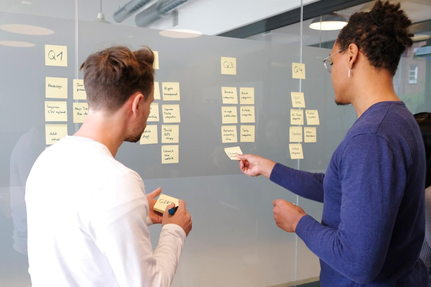 Zwei Männer kleben Notizen an eine Glaswand und planen eine Influencer Marketingstrategie.