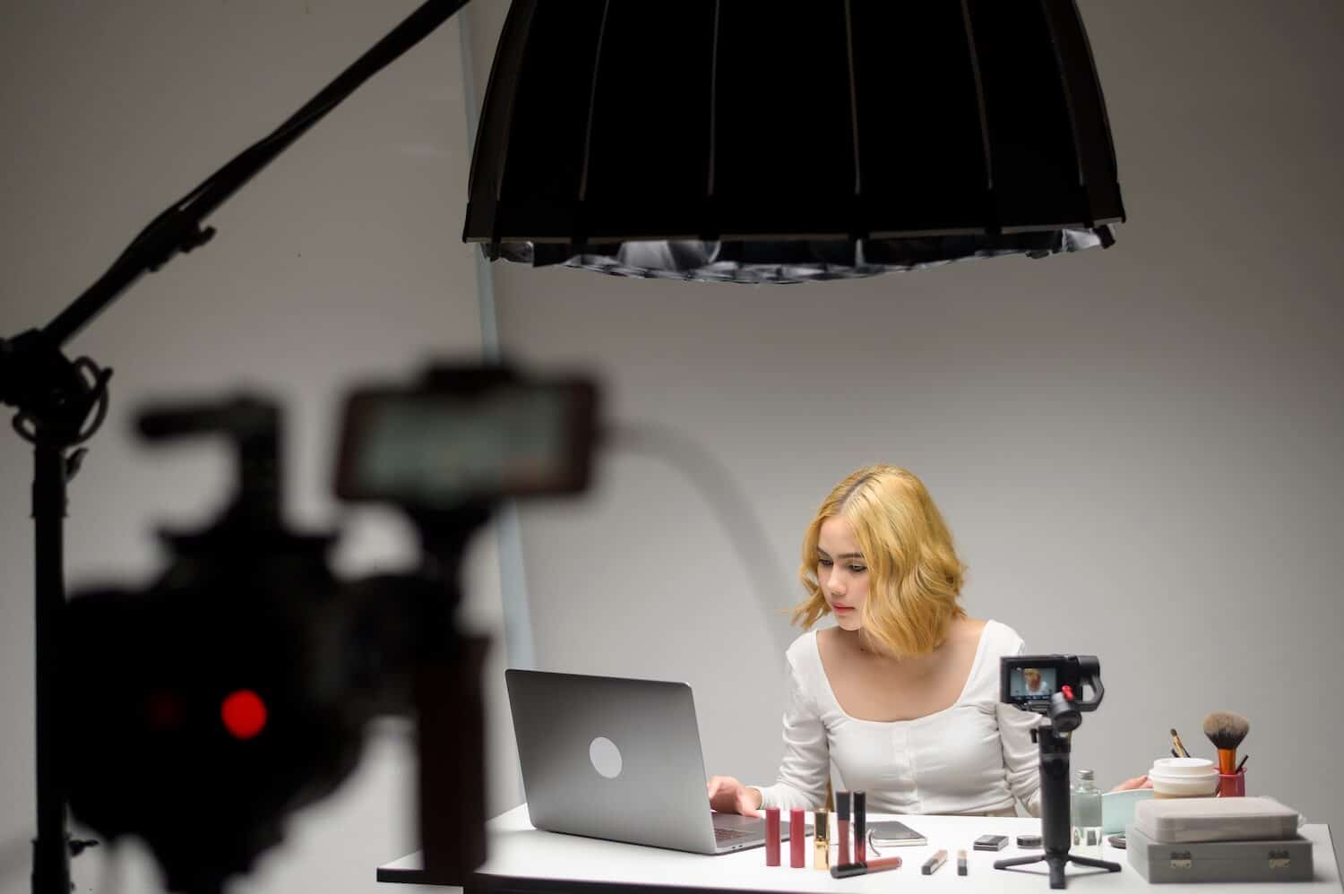 Eine Frau sitzt an einem Tisch mit einem Laptop und verschiedenen Produkten und produziert einen Livestream selbst.