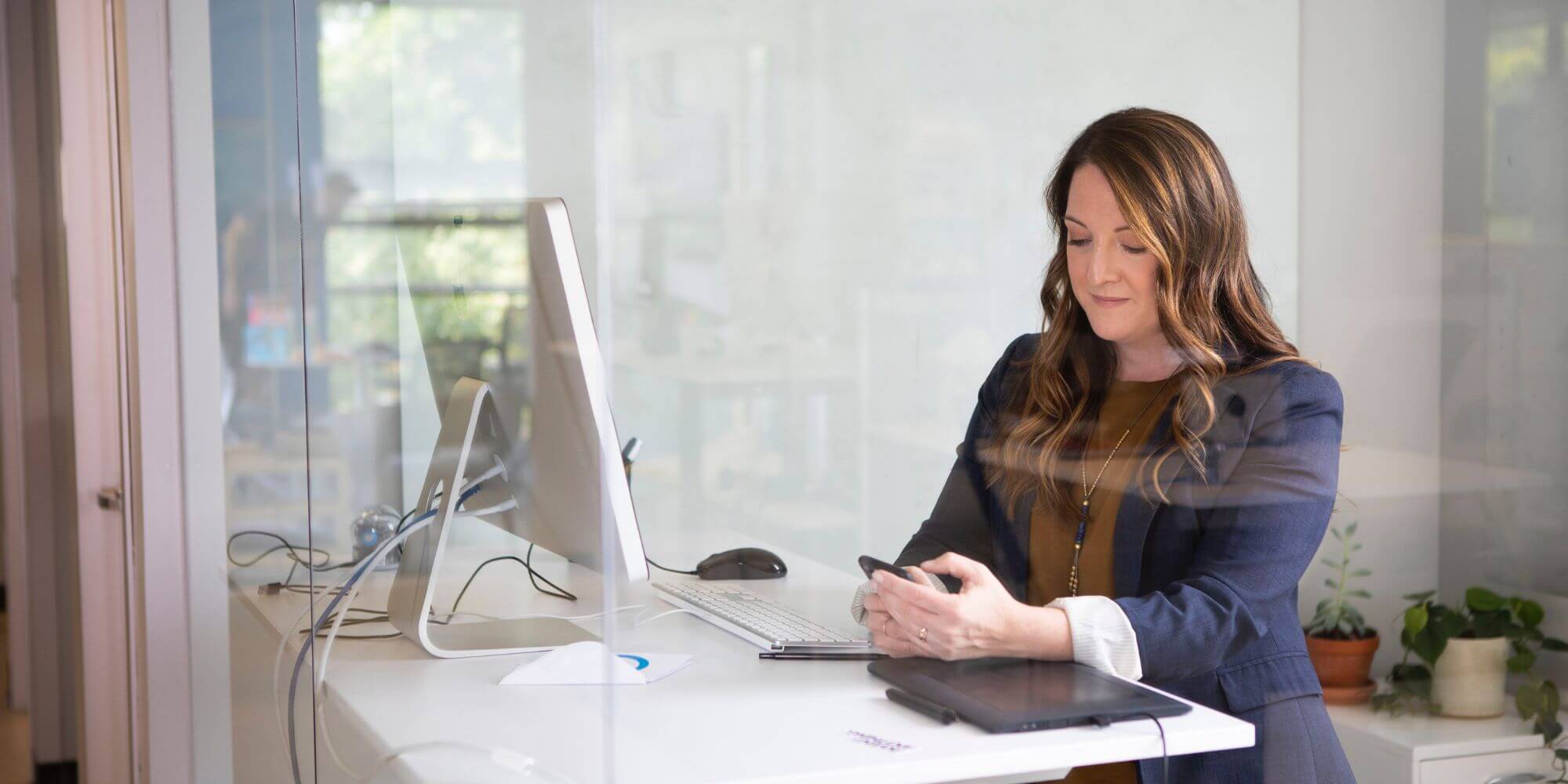 Frau steht in einem Büro am Schreibtisch und schaut auf ihr Smartphone