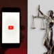 Ein Smartphone mit dem YouTube-Logo und eine Justitia-Figur