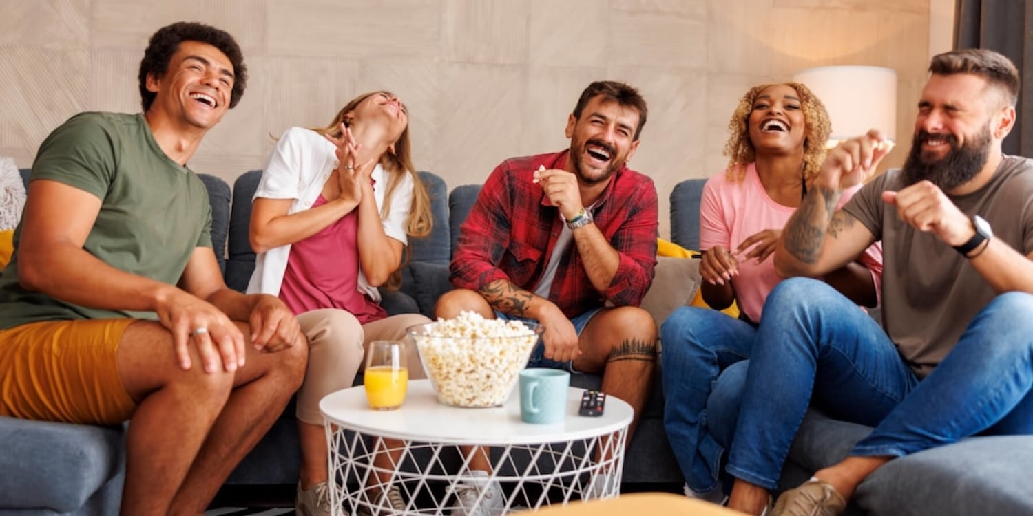  Fünf Freunde sitzen auf einer Couch, essen Popcorn und lachen über YouTube Fails.
