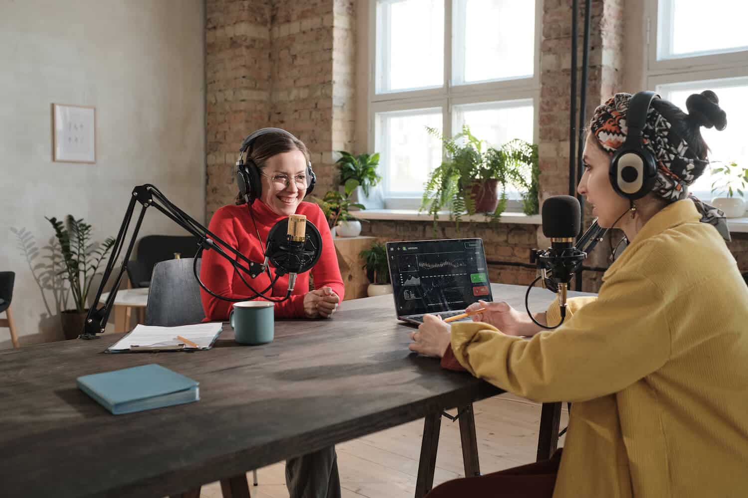 Zwei Frauen sitzen an einem Tisch und nehmen gemeinsam eine Podcast Episode auf.