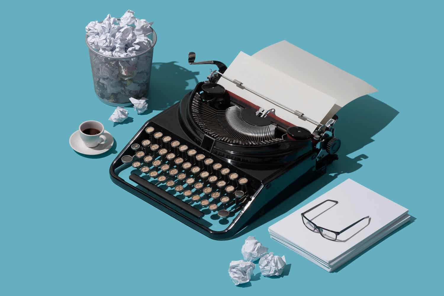 Eine Schreibmaschine, Mülltonne, Tasse und ein Stapel mit weißen Blättern auf einem blauen Hintergrund.