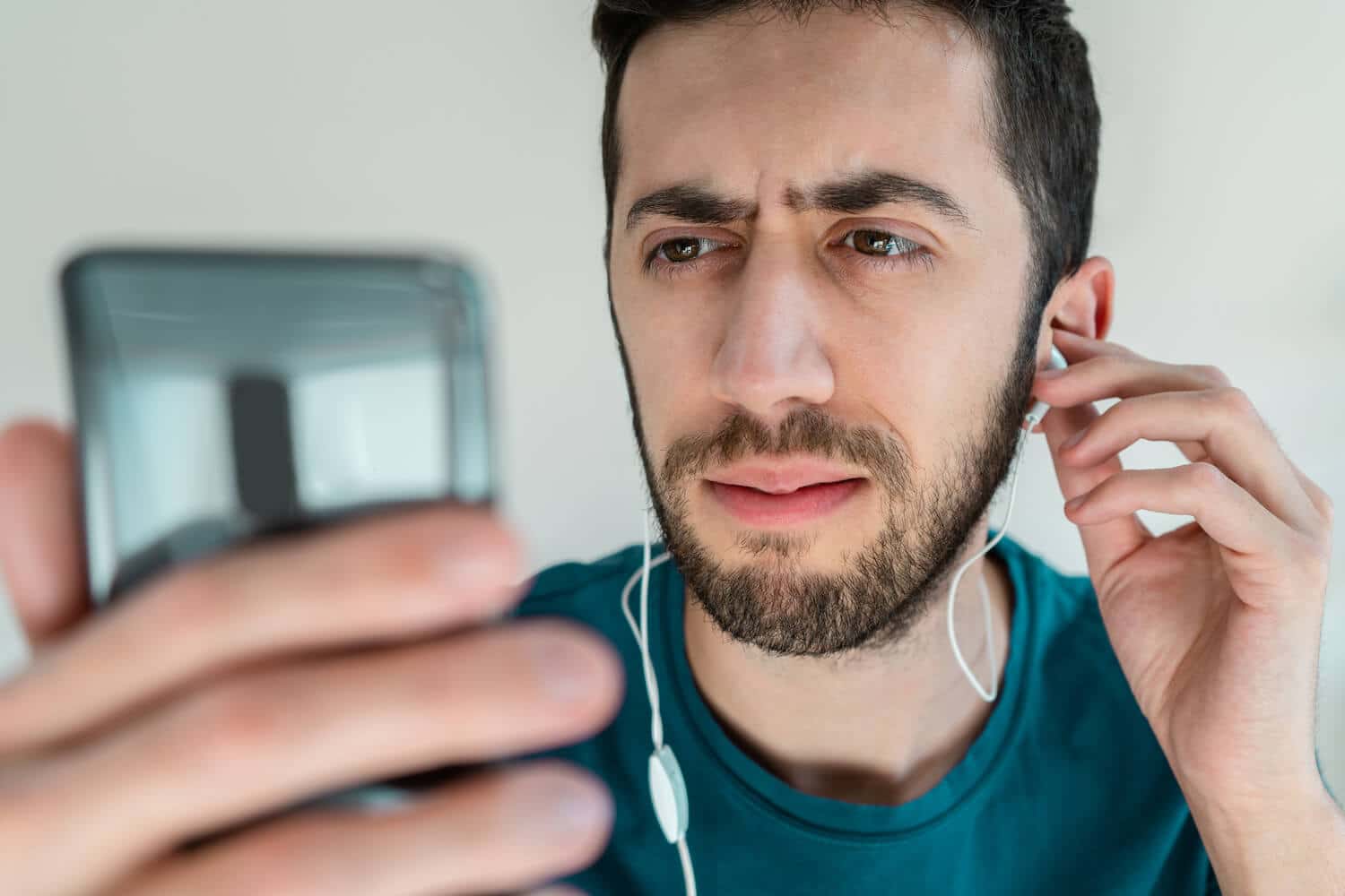 Ein Mann schaut eine Videoanleitung auf seinem Smartphone mit seinen Kopfhörern und ist unzufrieden.