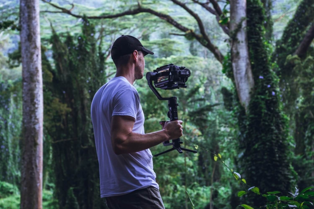 Ein Mann bewegt sich mit einer Handkamera durch die Natur und repräsentiert die nachhaltige Produktion von Filmen.